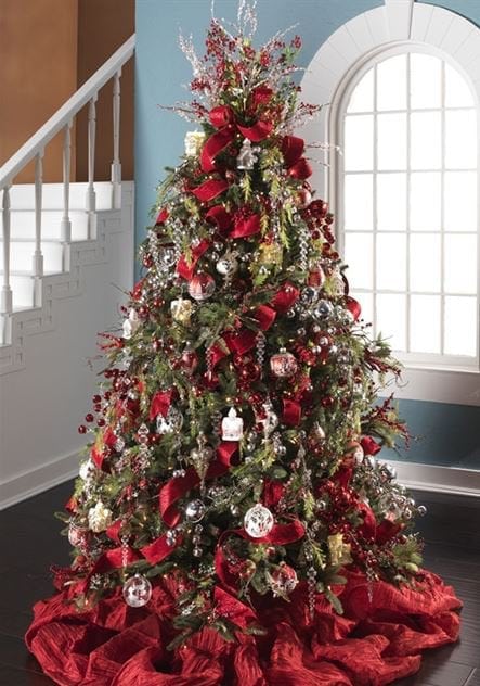 red ribbon, red ornament, bell picks and sprays, red tree skirt on a green tree