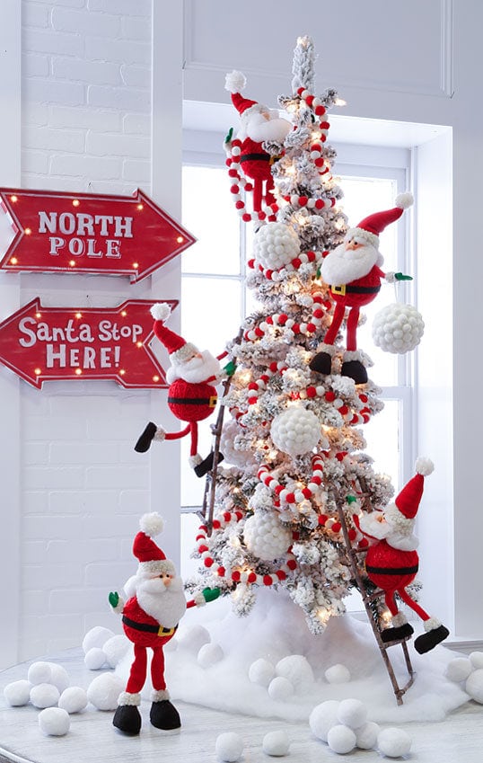 north pole village, pot bellied santas, huge snowball ornament and red and white garland on a flocked tree