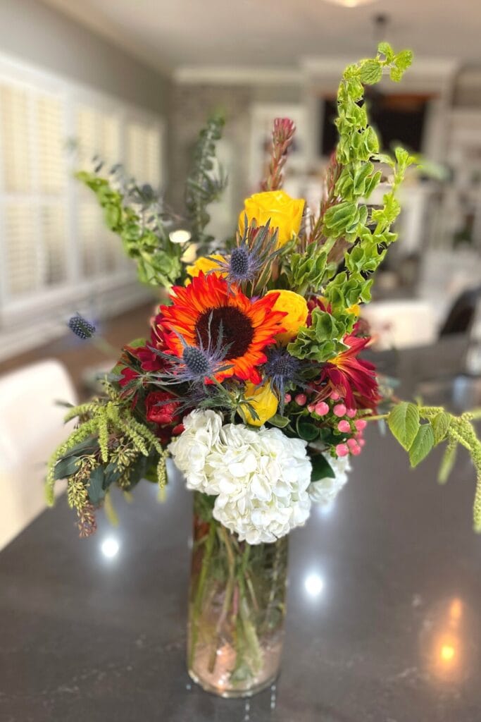 reddish orange sunflower, bells of ireland in a clear glass vase