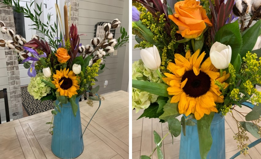 Blue watering can container with fresh golden yellow sunflowers, white tulips, orange roses, cattails and cotton boll stems