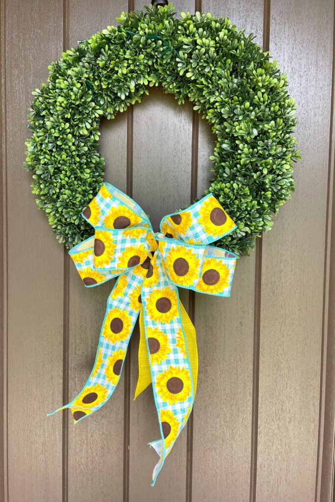 plastic boxwood wreath on front door with sunflower bow