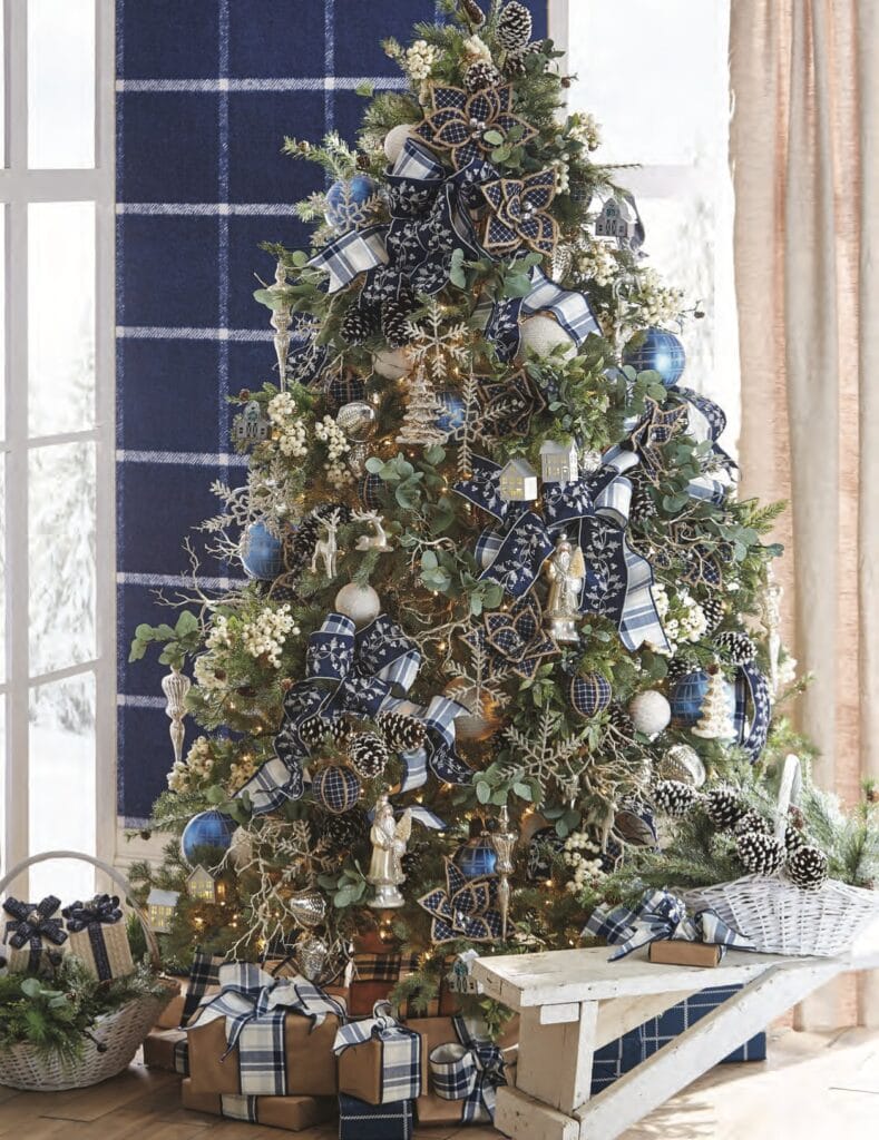 The Cozy Christmas tree is a little different with more “out of the box” thinking. If you’ve ever tried your hand at having a “blue” Christmas tree, you will remember how much trouble it was trying to “match” the blues. Well, you don’t have to! This tree has shades of royal, navy, a bit of faded denim, and even a hint of turquoise. I think the eucalyptus sprays tone down the blue with their gray-green color.

Blue poinsettias might be a bit harder to find than red, white, or gold, but they are out there! I know Trendy Tree is out of them right now, but they will have more in stock later. This is a huge tree! Big frosted pinecones and big ornaments. Lots of ribbon too! Don’t be afraid to mix your plaids and patterns on your tree.

Brown paper packages with matching ribbons carry the theme right down to the floor! The brown paper packaging also complements the twig branches in the tree and the poinsettias with natural-colored edging.