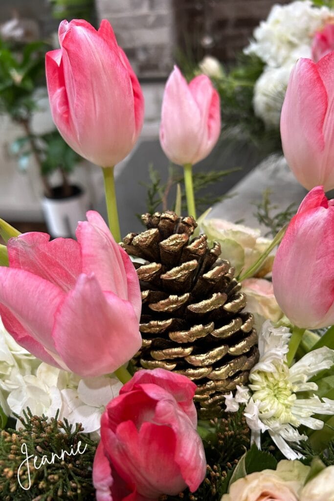 pink tulips in a vase with a gold pinecone and snowflake mums