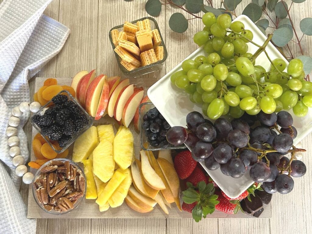 charcuterie board with pineapple, pecans, pears, apples strawberries, blackberries, blueberries, grapes, sugar wafer cookies