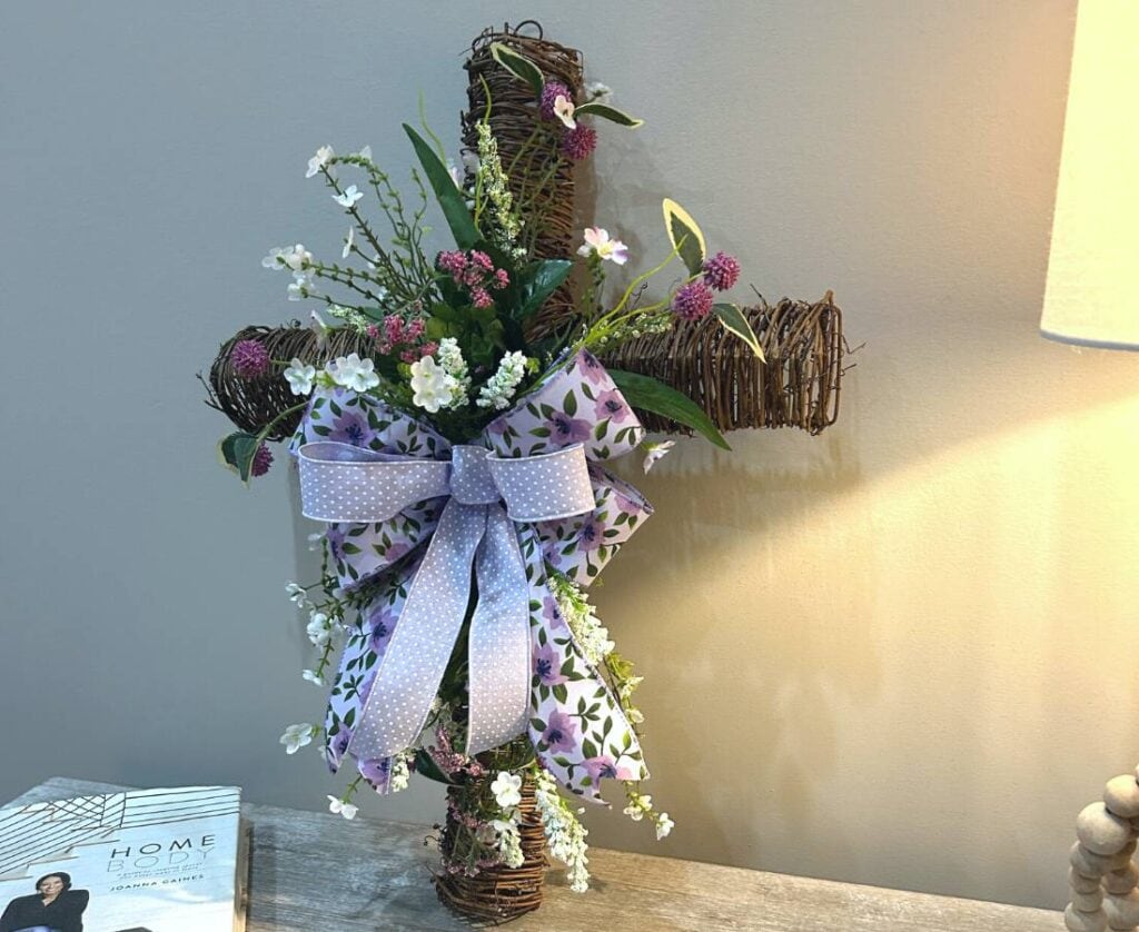 twig cross with flowers and a bow on a interior table