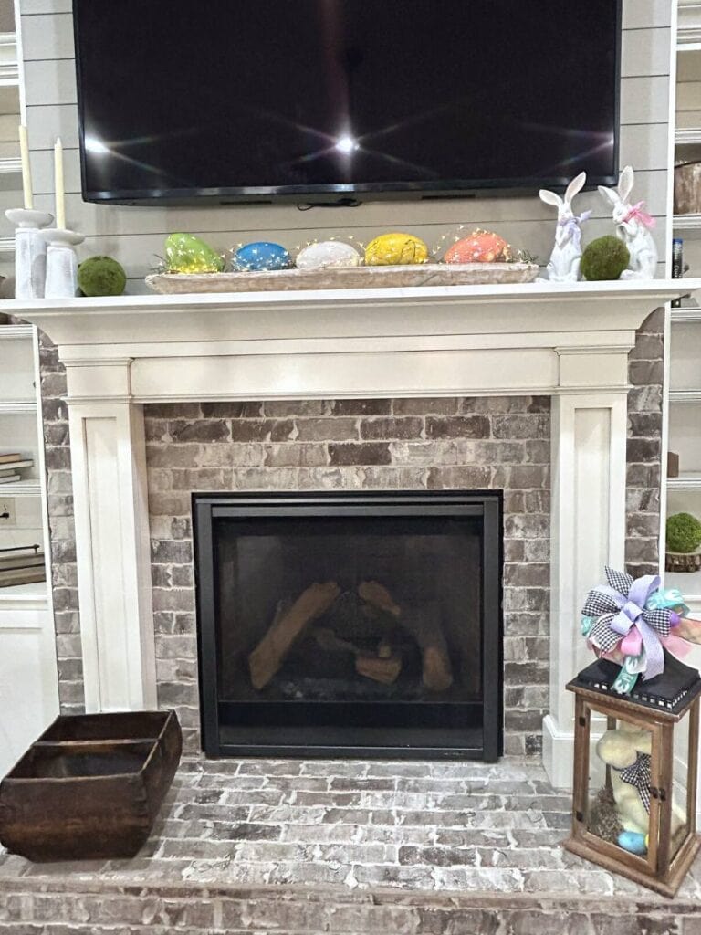 mantel decorated with easter eggs, bunnies and candles with lantern on the hearth, flocked bunny with funky bow on top