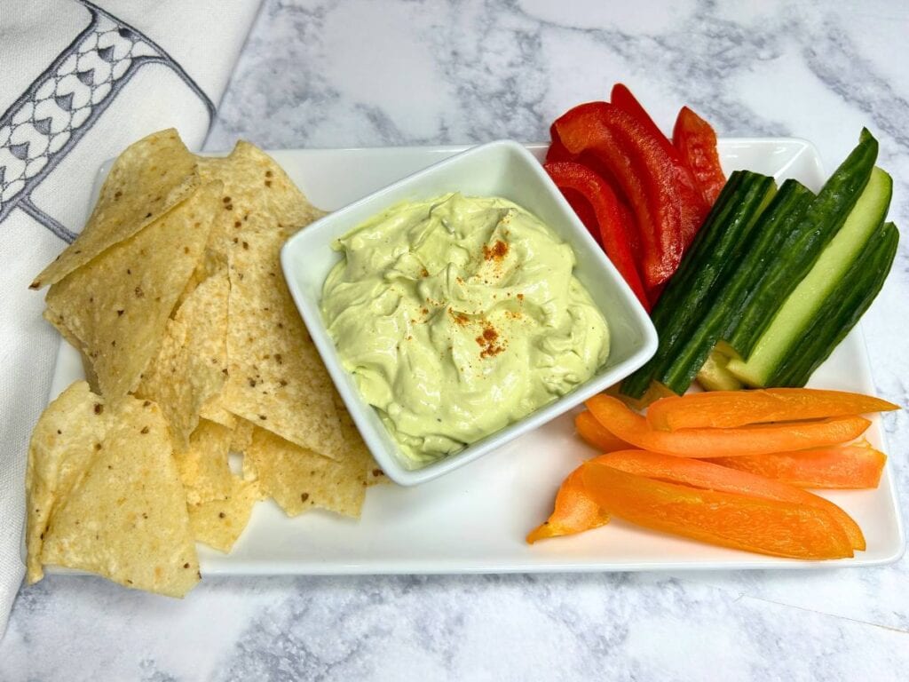 snack plate with avocado veggie dip, chips, pepper strips and cucumber slices