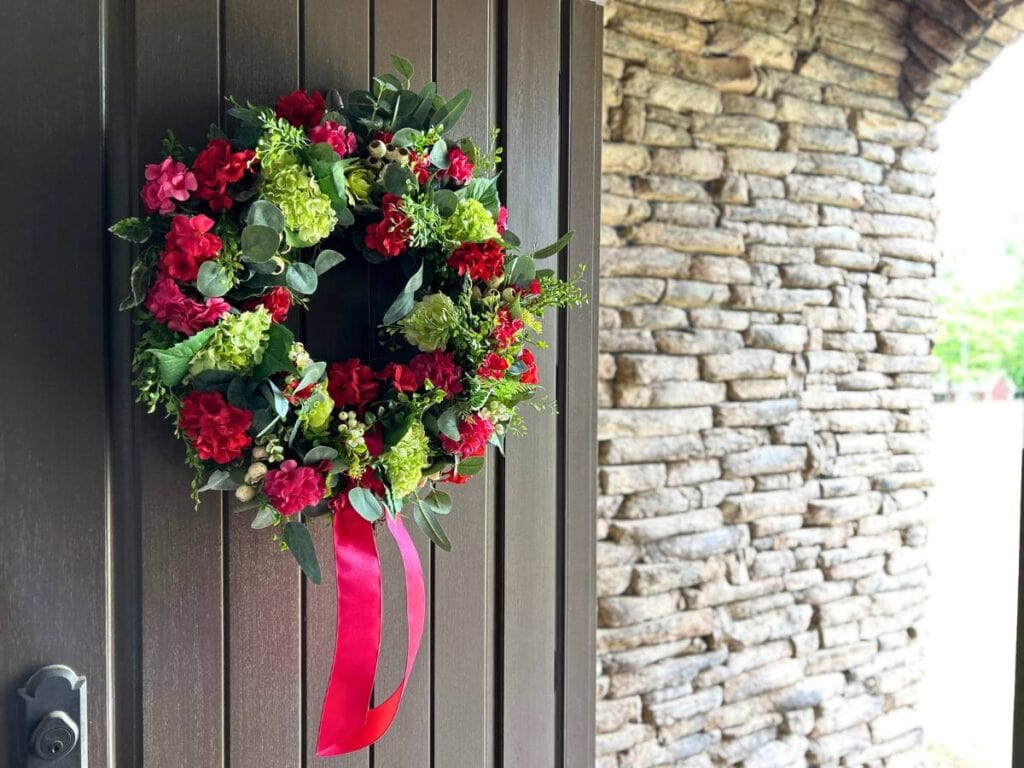 spring and summer wreath hanging on a front door blooms in red, deep pink and lime green, simple ribbon tied in a knot