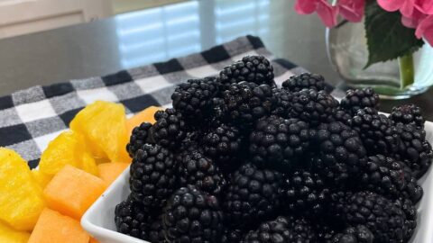 fresh blackberries in a white bowl beside chopped fruit
