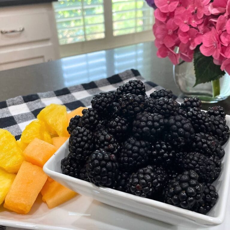 fresh blackberries in a white bowl beside chopped fruit