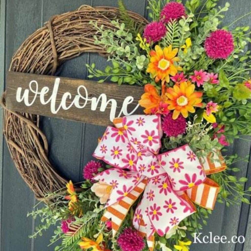 welcome wreath with spring flowers like peach blossoms and daisies and a bow made with two styles of ribbon