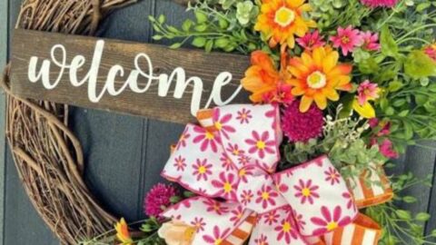 welcome wreath with spring flowers like peach blossoms and daisies and a bow made with two styles of ribbon