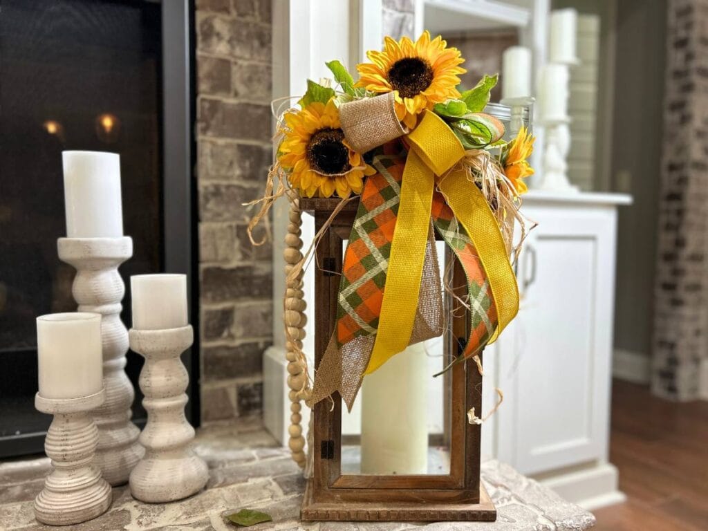 lantern on fireplace hearth decorated with a sunflowers, ribbon, raffia and wood beads