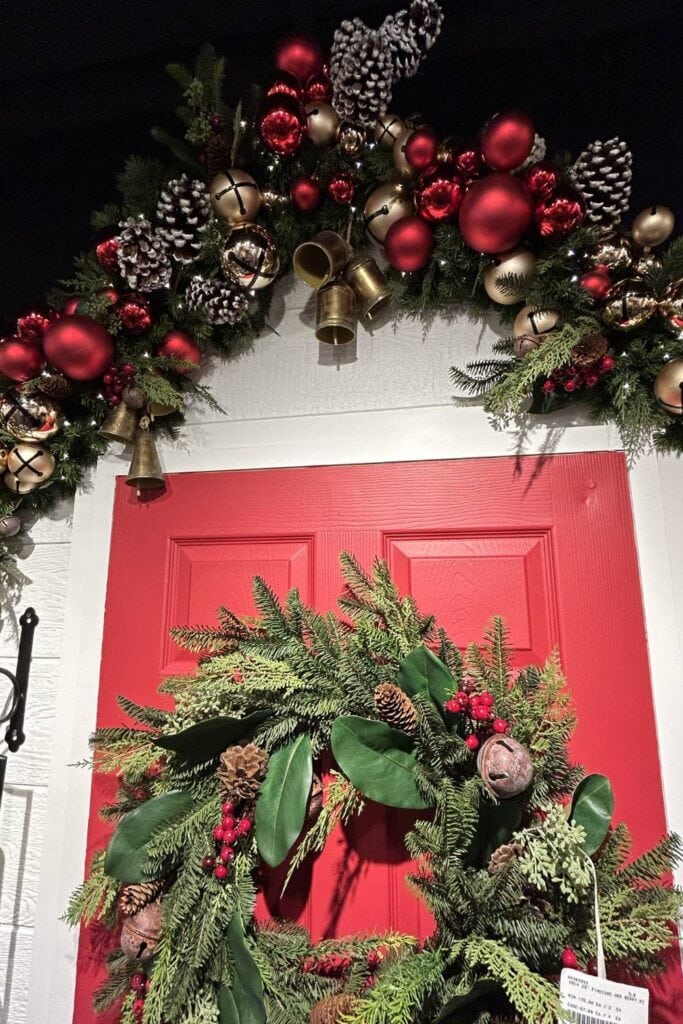 evergreen garland above a door decorated with red balls and baubles, bells and frosted pinecones