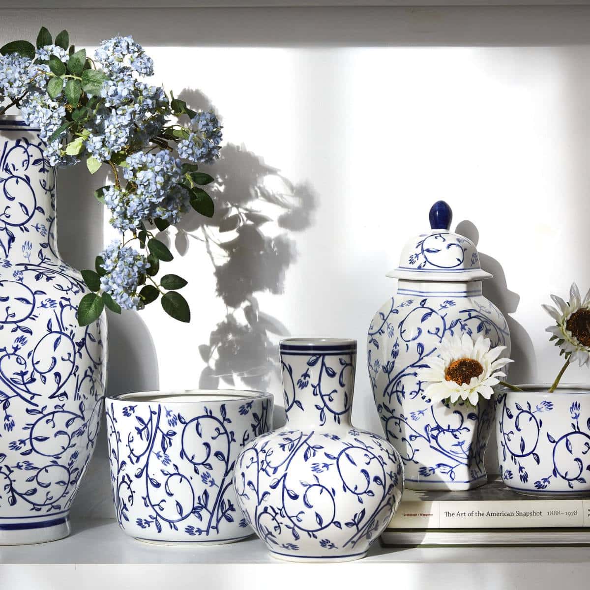 collection of white and blue pottery, some sitting on a stack of books as a riser