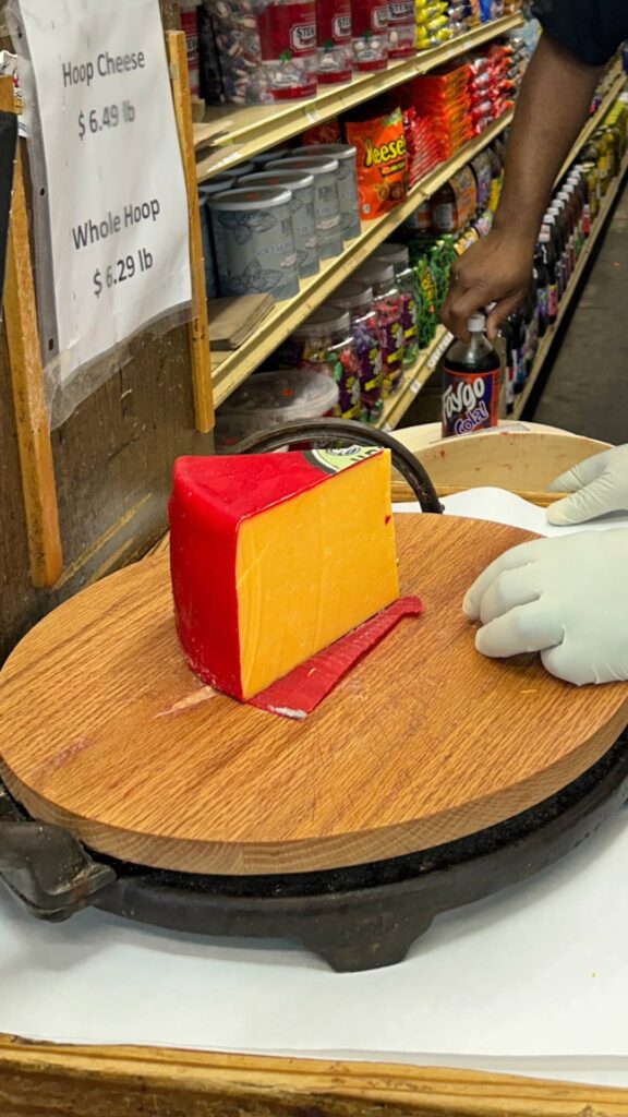 a slice of red waxed rind hoop cheese being cut with a huge cutter