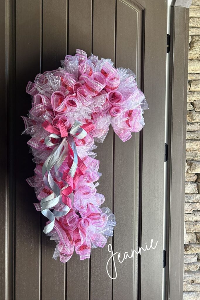 front door wreath made with pink, red, white stripped deco mesh and white snowed mesh, simple pink and white velvet bow