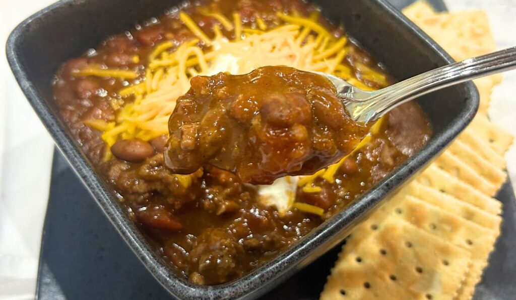 bowl of chili with crackers, chili topped with a dolop of sour cream and shredded sharp cheddar cheese