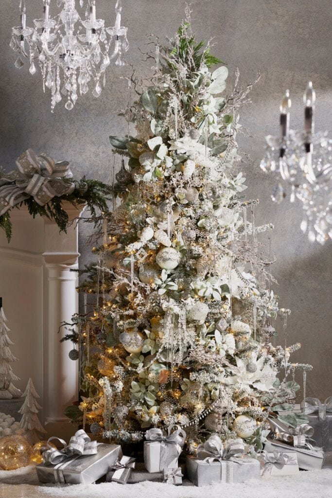 The "Snowflake Soiree" tree has a beautiful, snowy look with silver, white, and soft green decorations. It's covered in icy branches, glittering ornaments, and elegant flowers. Warm lights add a soft glow, and silver-wrapped presents sit underneath. The tree creates a glamorous winter wonderland feel, perfect for a sophisticated holiday setting.