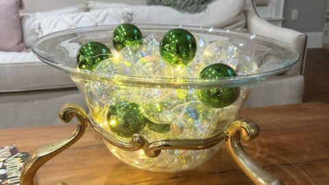 clear glass bowl on a gold stand filled with glass ball and twinkle lights
