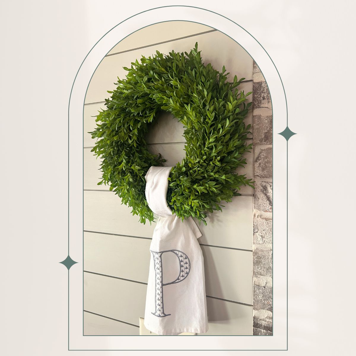 green boxwood wreath with a monogrammed tea towel used as a wreath sash