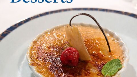 Crème brûlée dessert served on a cruise ship dining table with caramelized sugar topping, raspberry, mint leaf, and chocolate garnish.