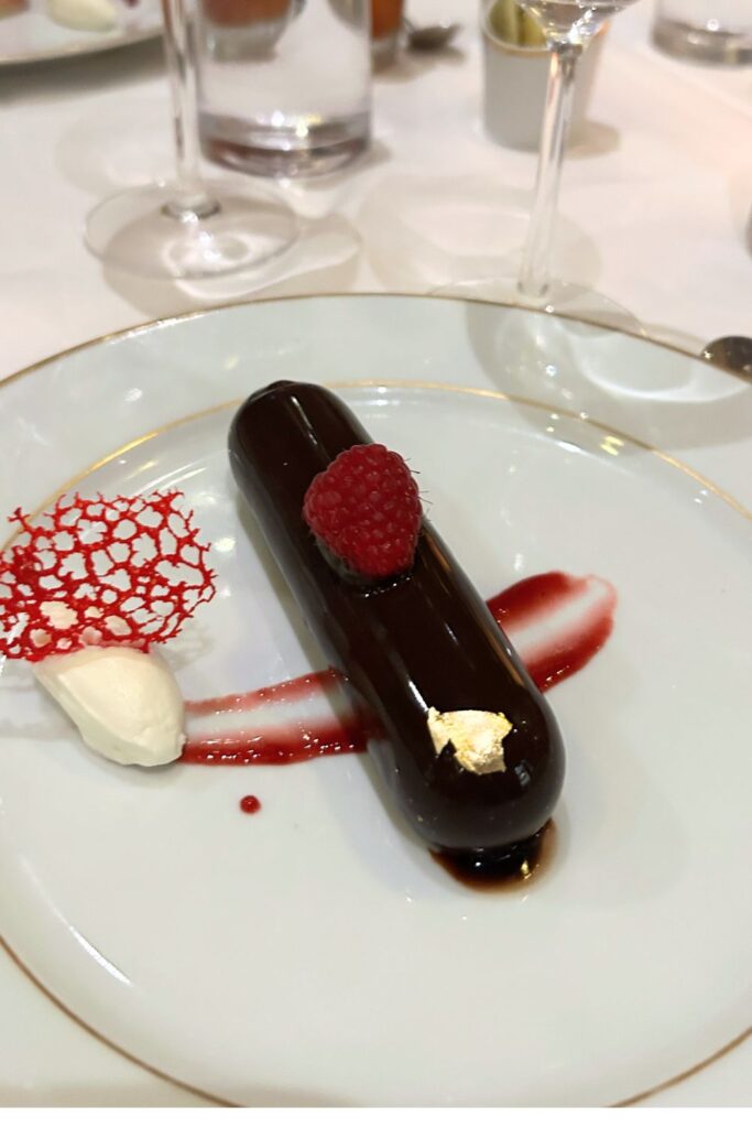 Chocolate cannoli-style dessert with glossy chocolate glaze, raspberry, and cream garnish served in the cruise ship dining room.