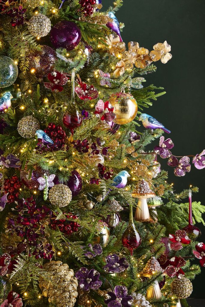 Christmas tree decorated with jewel-toned ornaments in burgundy, plum, and gold with birds, butterflies, florals, and mushroom ornaments in an enchanted forest theme.
