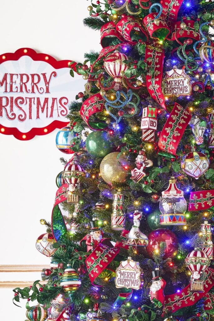 Colorful Christmas tree decorated with red ribbon, bright ornaments, carnival-style figures, and multicolor lights in the Holiday Spectacular theme.